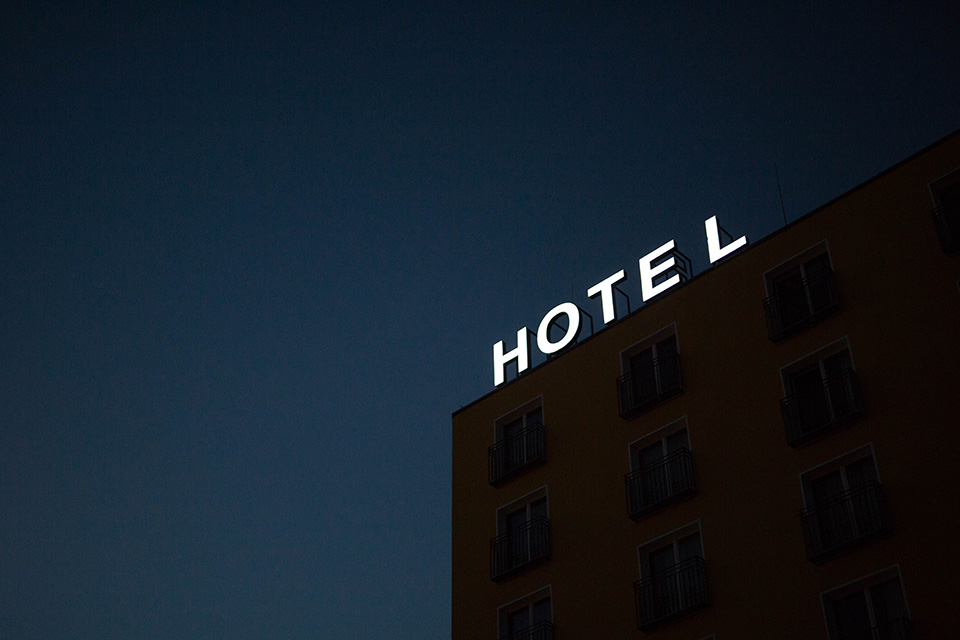 Looking up towards the night sky, with the top of a hotel appearing in the lower-right quadrant, and letters spelling 'HOTEL' on its roof.